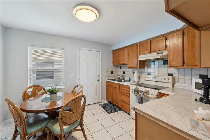 Kitchen featuring under cabinet range hood, white electric range oven, light countertops, a sink, and tasteful backsplash