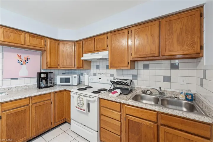 Kitchen featuring white appliances, under cabinet range hood, a sink, light countertops, and tasteful backsplash