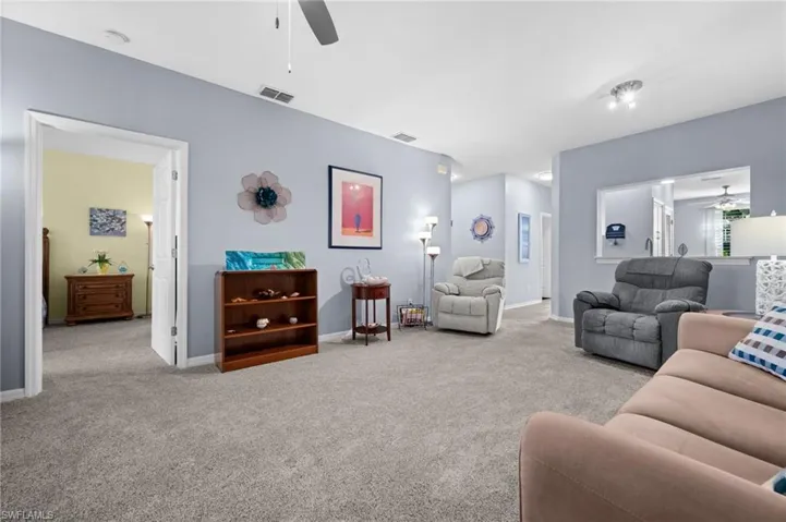 Neutral-toned wall-to-wall carpeting throughout, a ceiling fan with integrated lighting, and a pass-through window detail