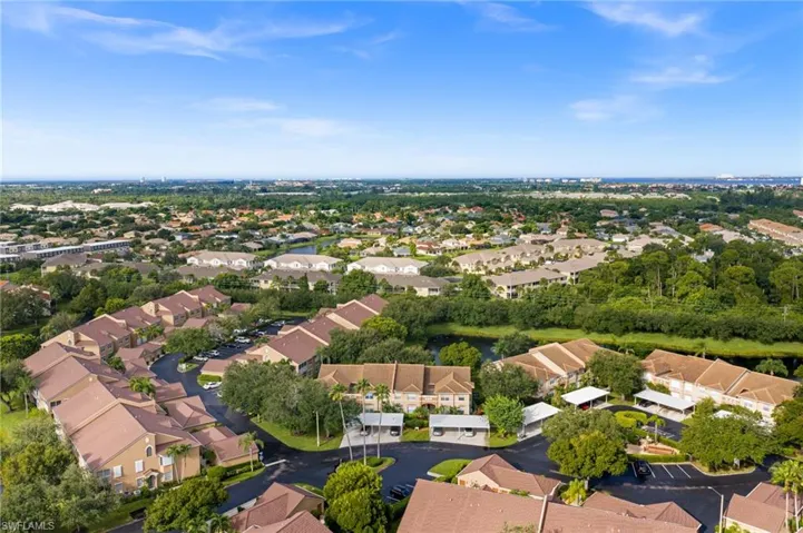 Expansive aerial perspective showcasing a residential community with abundant green spaces, multiple residential buildings with tan roofs, and paved parking areas