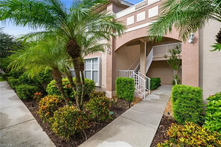 Building exterior featuring stucco finish, arched entryway, white railings, and mature tropical landscaping