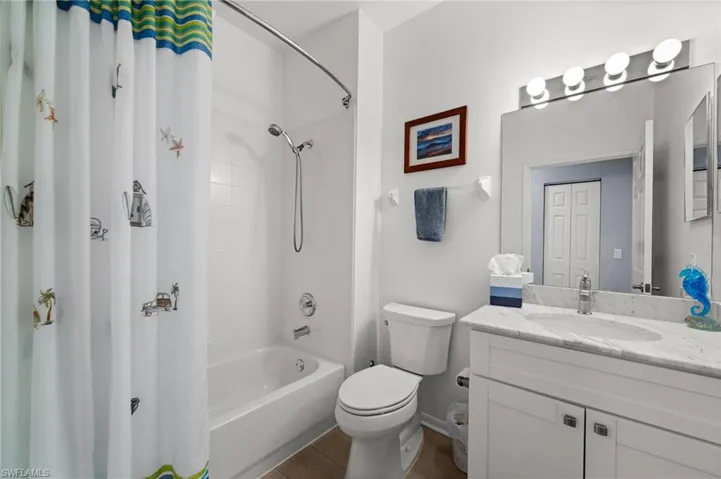 Bathroom featuring a single vanity with stone countertop, white cabinetry, integrated sink, and a combination tub and shower