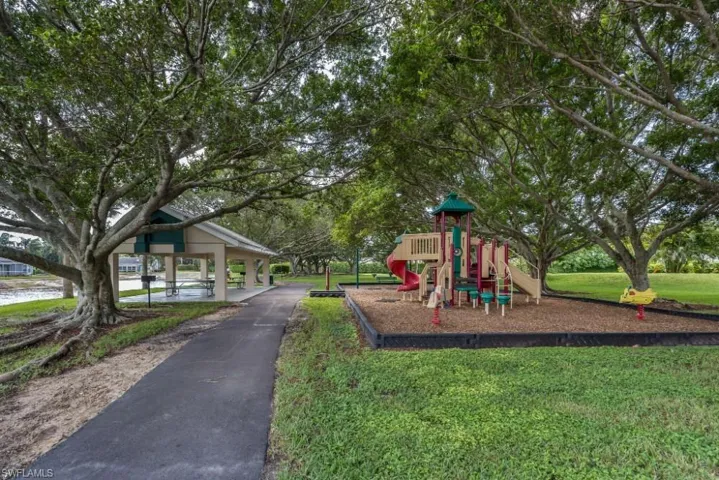 Community park with a playground structure, covered picnic area, paved pathway, and mature trees