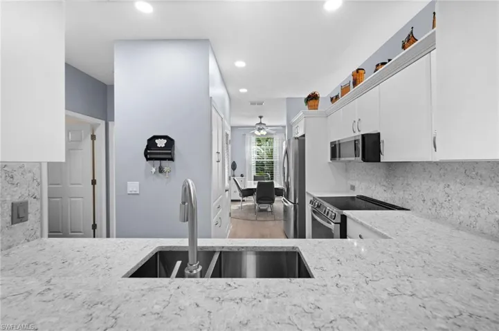Kitchen featuring light-toned countertops, undermount double-basin sink with a gooseneck faucet, white cabinetry, and stainless steel appliances
