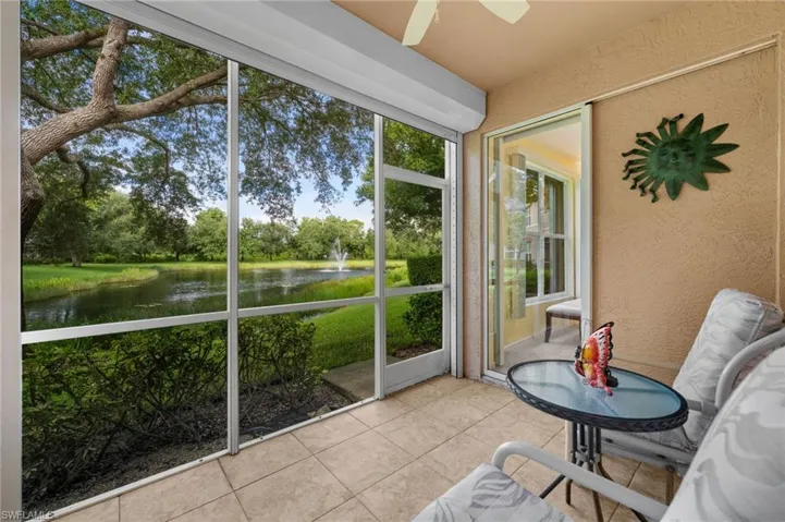 Screened lanai featuring a pond with a fountain, mature trees, and a beige tiled floor