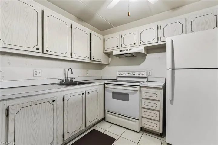 Kitchen with white appliances, light countertops, under cabinet range hood, light tile patterned floors, and ceiling fan