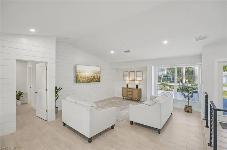 Living area with vaulted ceiling, wood walls, light wood-style floors, and recessed lighting