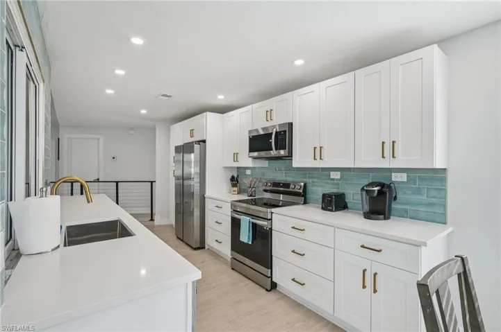 Kitchen with stainless steel appliances, decorative backsplash, recessed lighting, white cabinetry, and light countertops