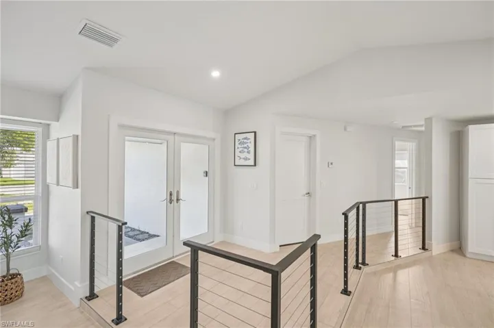 Hallway featuring an upstairs landing, lofted ceiling, light wood-style floors, recessed lighting, and french doors