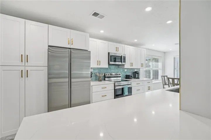 Kitchen featuring stainless steel appliances, white cabinetry, recessed lighting, decorative backsplash, and light stone countertops