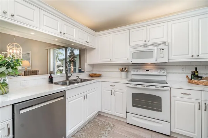 Kitchen with white appliances, white cabinetry, backsplash, and light stone countertops