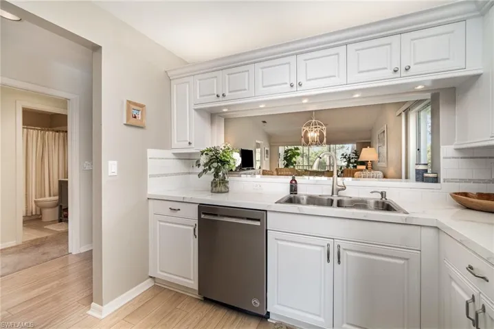 Kitchen with tasteful backsplash, light countertops, stainless steel dishwasher, white cabinets, and light wood-style flooring