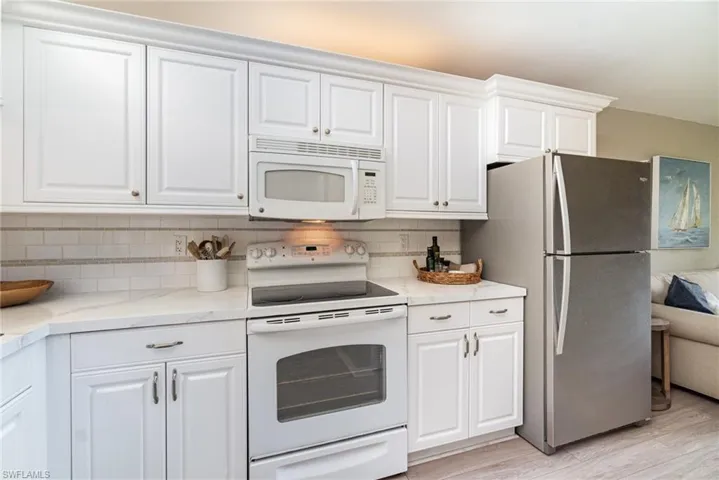 Kitchen with white appliances, white cabinets, light stone counters, and light wood-style flooring