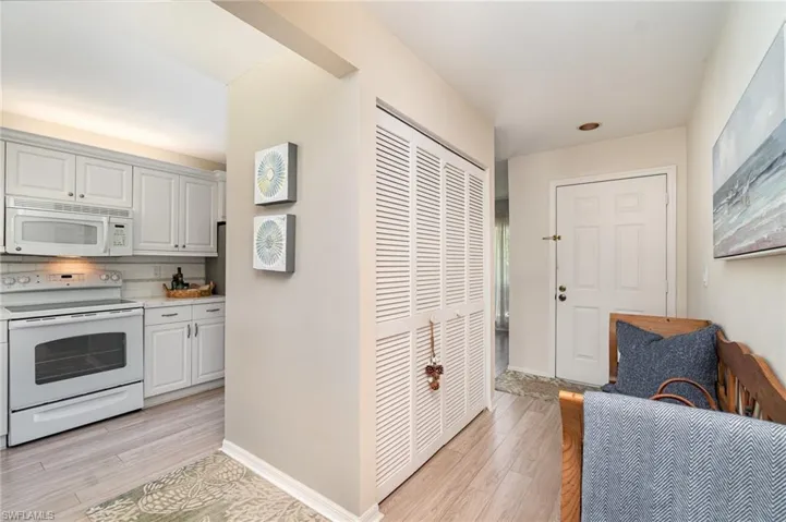 Kitchen featuring white appliances, light wood-style flooring, light countertops, backsplash, and white cabinetry