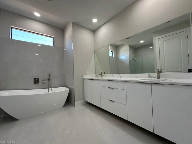 Bathroom featuring tile flooring, a tub, tile walls, large vanity, and dual sinks