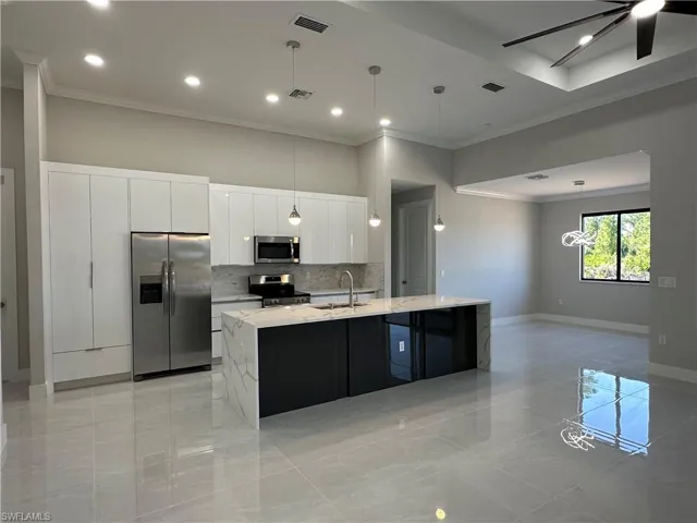 Kitchen featuring ceiling fan, an island with sink, stainless steel appliances, decorative light fixtures, and white cabinetry