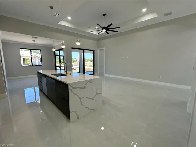 Kitchen with hanging light fixtures, a tray ceiling, a kitchen island with sink, sink, and light tile floors