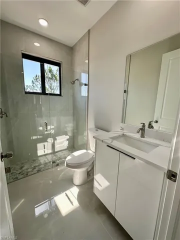 Bathroom featuring walk in shower, tile flooring, vanity, and toilet