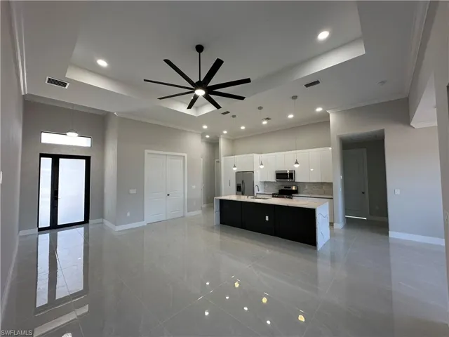 Kitchen with ceiling fan, an island with sink, pendant lighting, a raised ceiling, and white cabinetry