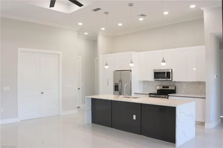 Kitchen with stainless steel appliances, ceiling fan, a kitchen island with sink, white cabinets, and light tile floors