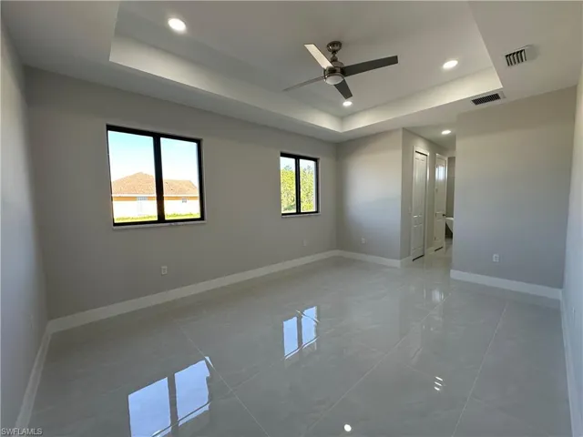 Tiled empty room featuring ceiling fan and a raised ceiling