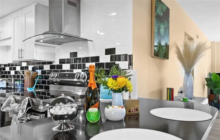 Kitchen with range hood, decorative backsplash, white cabinets, stainless steel range with electric stovetop, and wood finished floors