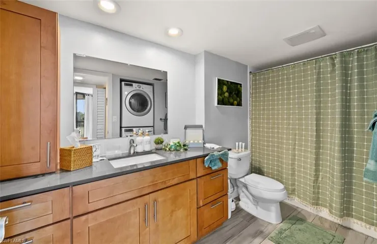 Bathroom with vanity, light wood-style flooring, stacked washing machine and dryer, recessed lighting, and shower / tub combo