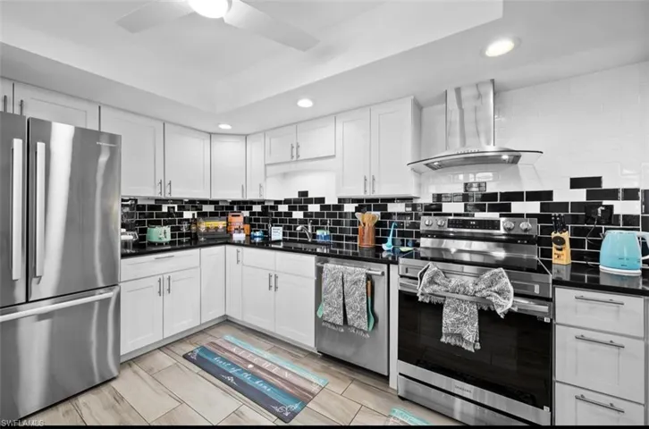Kitchen featuring stainless steel appliances, recessed lighting, white cabinets, wall chimney exhaust hood, and dark stone countertops