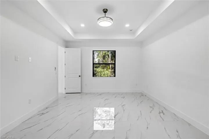 Empty room with light marble finish flooring, a tray ceiling, and recessed lighting