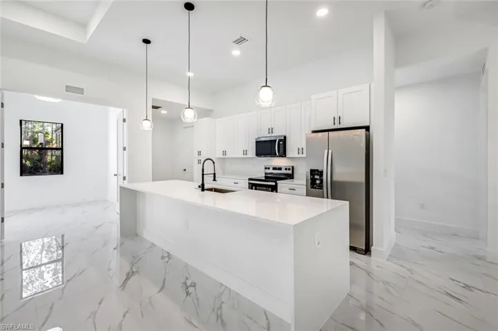 Kitchen featuring light stone counters, stainless steel appliances, pendant lighting, white cabinetry, and a center island with sink