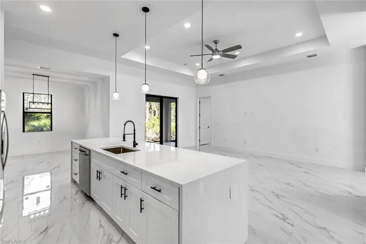 Kitchen with hanging light fixtures, white cabinetry, light stone countertops, a tray ceiling, and a kitchen island with sink