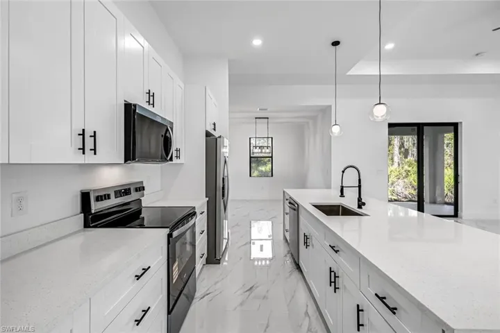 Kitchen with stainless steel appliances, light stone counters, and a large island with sink