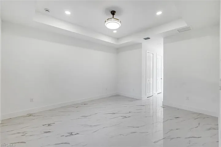 Spare room featuring a raised ceiling, recessed lighting, and light marble finish floors