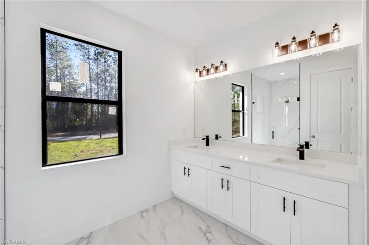 Bathroom with double vanity, light marble finish floors, and a marble finish shower