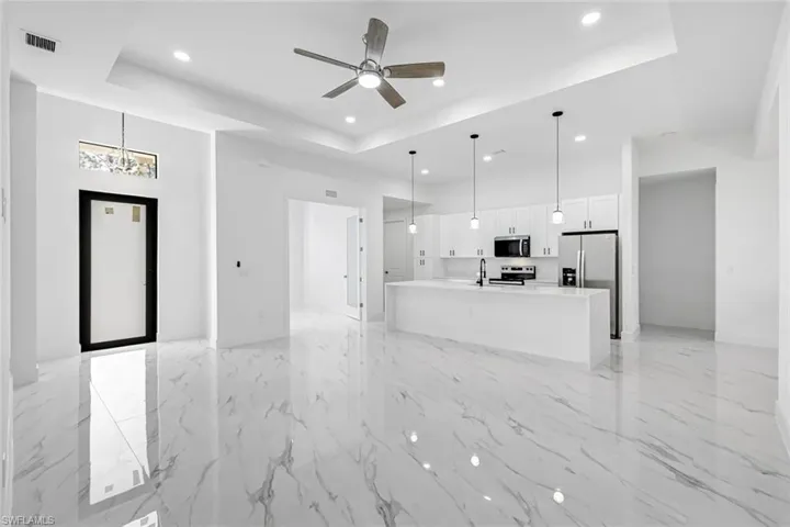 Unfurnished living room with a ceiling fan, recessed lighting, a high tray ceiling, and light marble finish floors