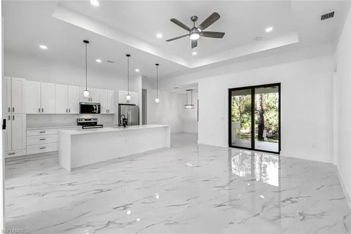 Kitchen with open floor plan, a center island with sink, white cabinetry, pendant lighting, and a ceiling fan