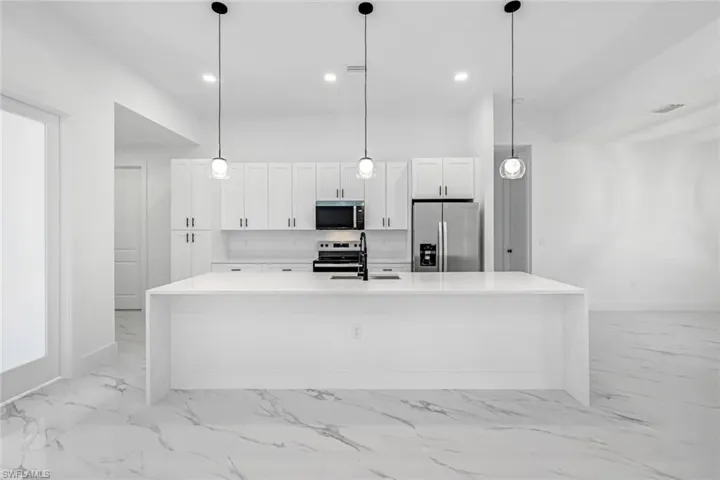 Kitchen featuring stainless steel appliances, light stone counters, decorative light fixtures, white cabinetry, and a spacious island