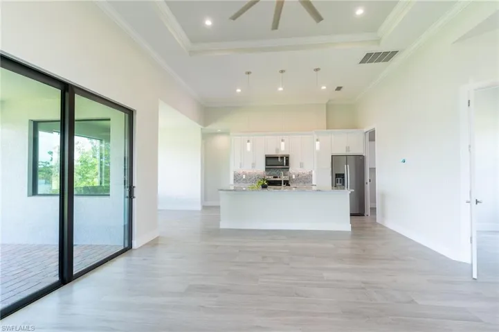 Kitchen with white cabinets, a kitchen island with sink, a tray ceiling, appliances with stainless steel finishes, and decorative backsplash