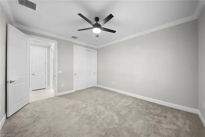 Unfurnished bedroom with ornamental molding, light carpet, a ceiling fan, and a closet
