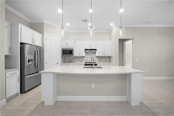 Kitchen with stainless steel appliances, white cabinets, pendant lighting, an island with sink, and ornamental molding