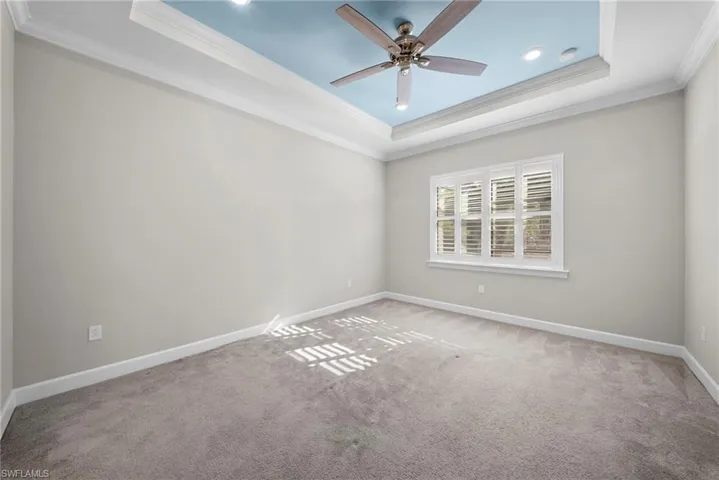 Carpeted spare room featuring ceiling fan, crown molding, and a tray ceiling