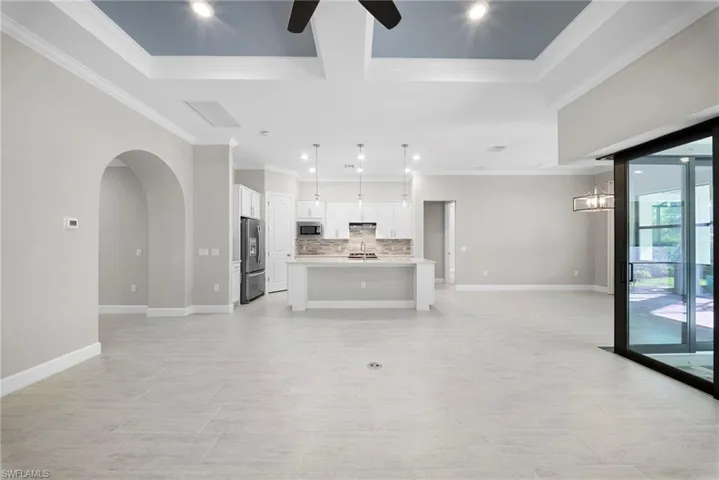 Unfurnished living room featuring arched walkways, a ceiling fan, recessed lighting, and ornamental molding