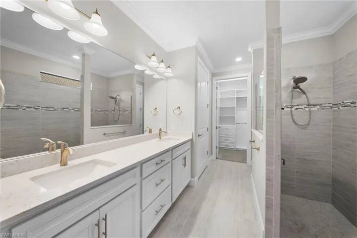 Bathroom featuring double vanity, tiled shower, a spacious closet, and ornamental molding