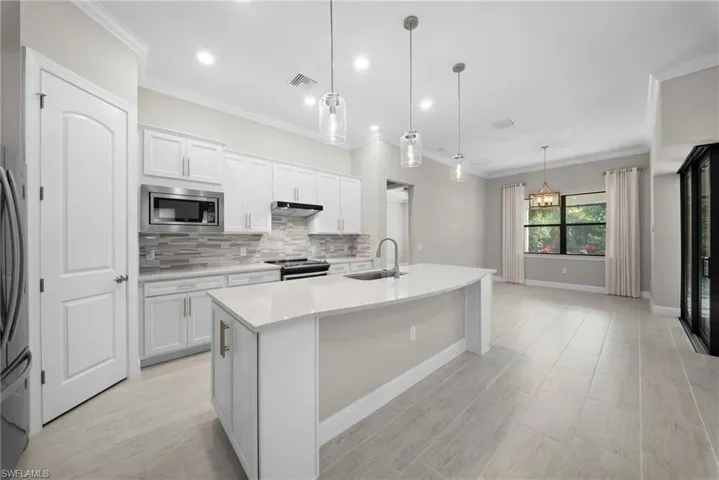 Kitchen with backsplash, a kitchen island with sink, white cabinetry, stainless steel appliances, and ornamental molding