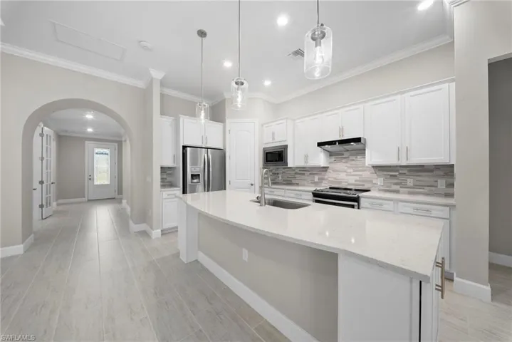 Kitchen featuring decorative backsplash, arched walkways, stainless steel appliances, white cabinetry, and ornamental molding