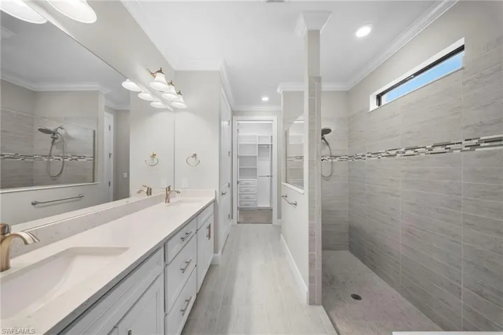 Full bathroom with a walk in shower, double vanity, a walk in closet, crown molding, and recessed lighting