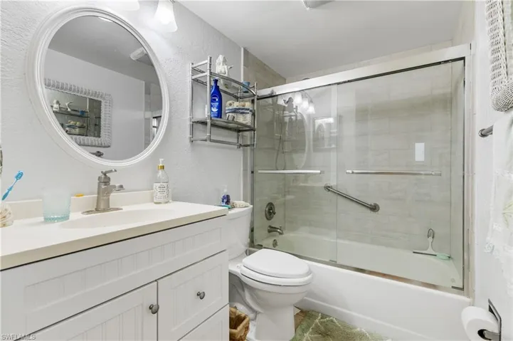Full bath with a textured wall, vanity, toilet, and enclosed tub / shower combo