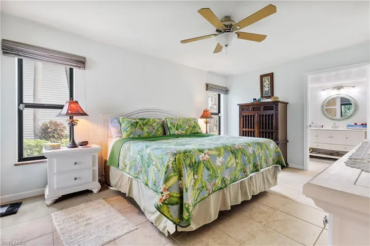 Bedroom with light tile patterned flooring, baseboards, ensuite bath, and a ceiling fan