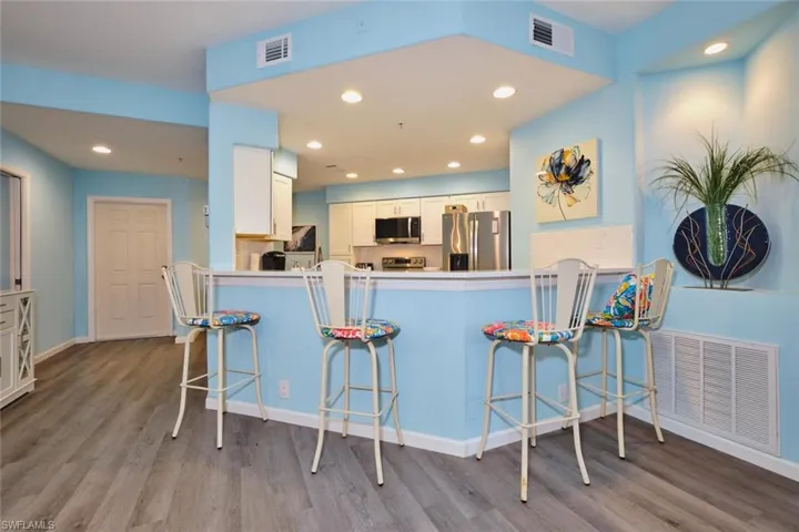 Kitchen with appliances with stainless steel finishes, wood finished floors, white cabinetry, a kitchen breakfast bar, and a peninsula