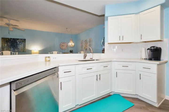Kitchen featuring stainless steel dishwasher, a ceiling fan, white cabinetry, decorative backsplash, and wood finished floors
